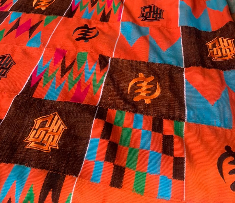 Orange Kente cloth with mechanical embroidery symbols